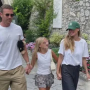Ilary Blasi e Bastian Müller tengono per mano una bambina con il volto oscurato, lungo un percorso fiorito.