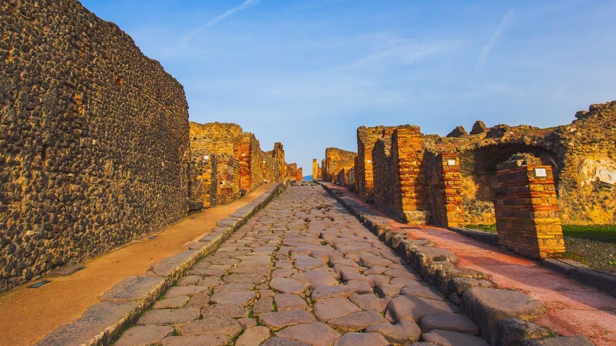Lunga strada romana lastricata attraversa le rovine di Pompei nella luce calda
